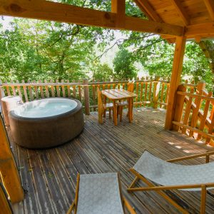 Cabane dans les arbres avec jacuzzi, terrasse en bois et chaises longues.