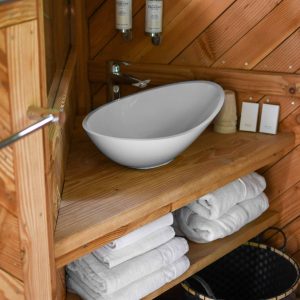 Salle de bain dun hébergement insolite en bois, avec lavabo moderne et serviettes blanches.