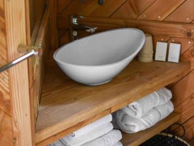 Salle de bain dun hébergement insolite en bois, avec lavabo moderne et serviettes blanches.