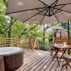 Cabane dans les arbres avec jacuzzi, terrasse en bois entourée de verdure.