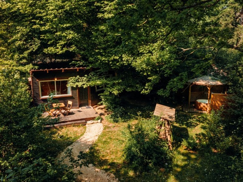 Cabane en bois nichée dans la verdure, avec une terrasse ensoleillée.