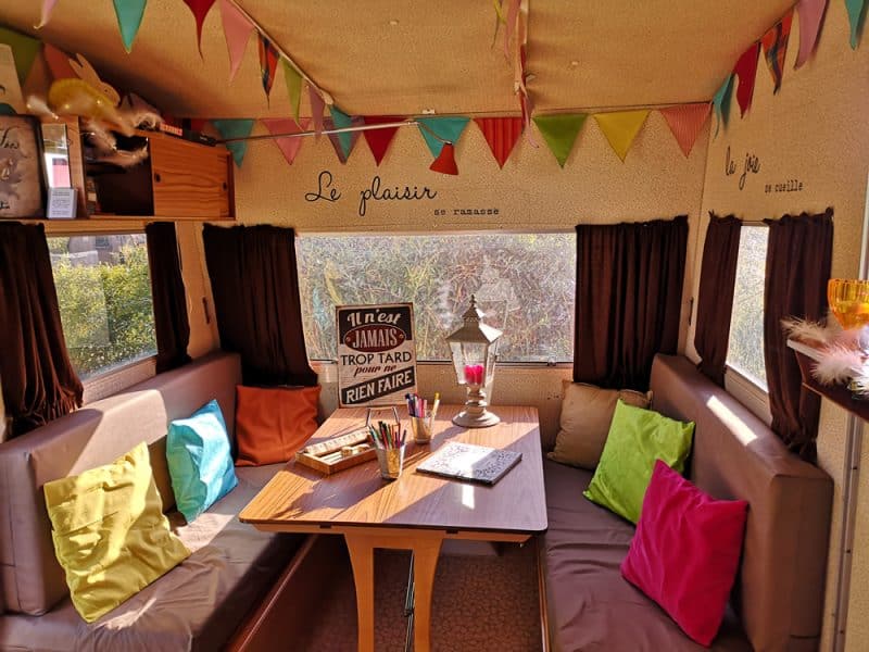 Caravane colorée avec coussins vifs et décorations festives, ambiance chaleureuse.