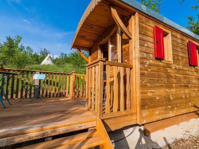 Cabane en bois avec terrasse, fenêtres rouges, au cœur de la nature en Auvergne-Rhône-Alpes.