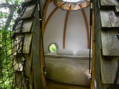 Cabane perchée dans les arbres, avec un lit douillet et des murs en bois.