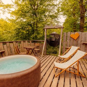 Cabane perchée en bois avec jacuzzi, entourée de verdure apaisante.