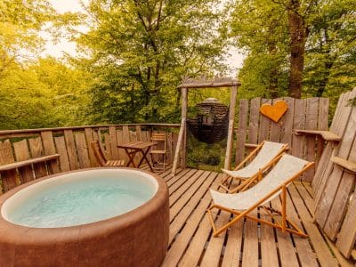 Cabane perchée en bois avec jacuzzi, entourée de verdure apaisante.