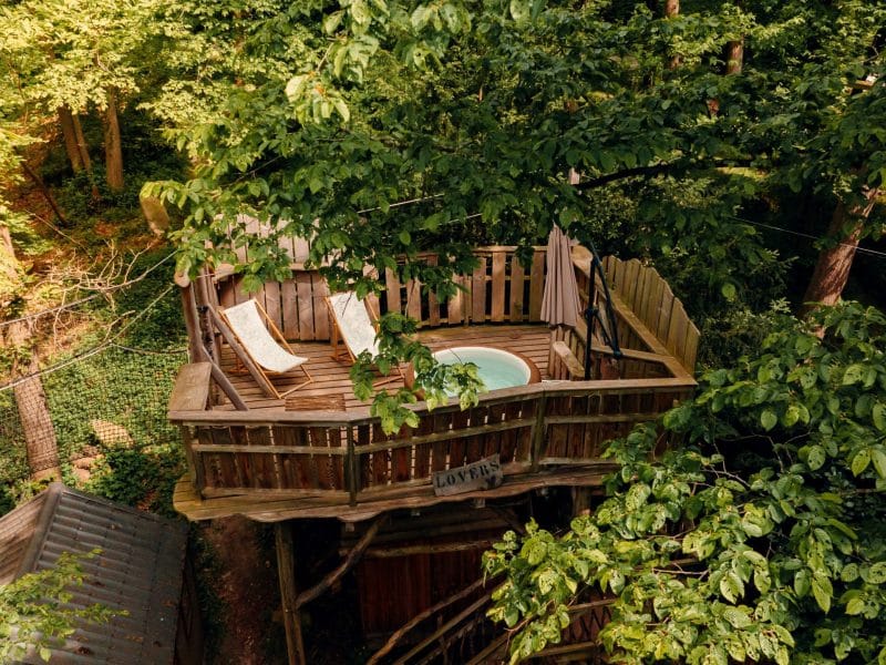 Cabane dans les arbres avec jacuzzi, entourée de verdure luxuriante.