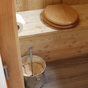 Toilettes sèches en bois dans un hébergement insolite, ambiance naturelle et chaleureuse.