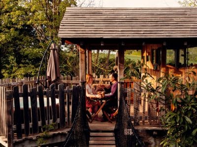 Cabane perchée dans les arbres, avec une passerelle suspendue et vue sur la nature.