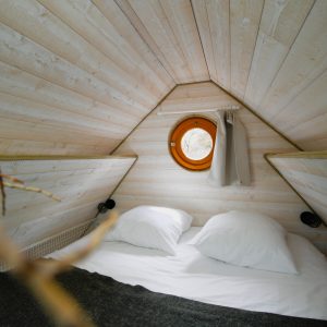 Cabane insolite en bois avec un lit douillet et une fenêtre ronde.