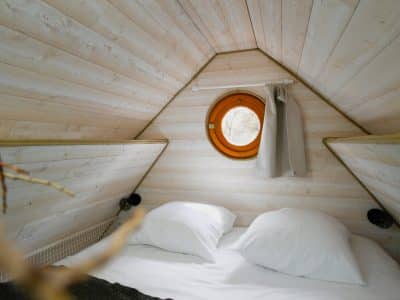 Cabane insolite en bois avec un lit douillet et une fenêtre ronde.