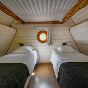 Chalet en bois avec lits jumeaux et fenêtre ronde, ambiance chaleureuse et cosy.
