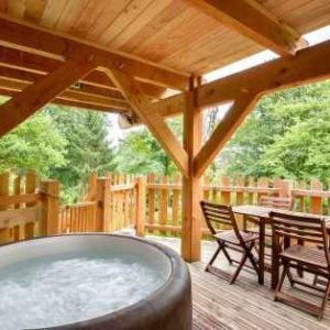 Cabane en bois avec jacuzzi, entourée de verdure, idéale pour un séjour relaxant.