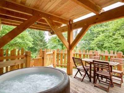 Cabane en bois avec jacuzzi, entourée de verdure, idéale pour un séjour relaxant.