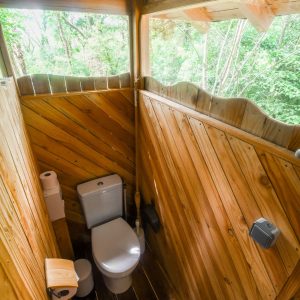 Toilettes en bois dans un hébergement insolite en Hauts-de-France, entourées de verdure.