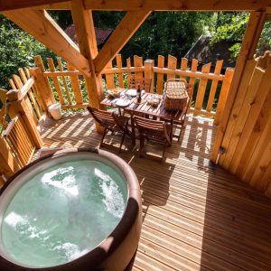 Cabane perchée avec jacuzzi, entourée de verdure et dune terrasse en bois.