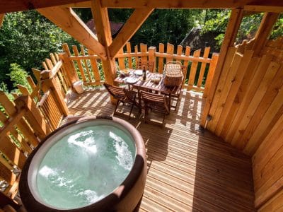Cabane perchée avec jacuzzi, entourée de verdure et dune terrasse en bois.