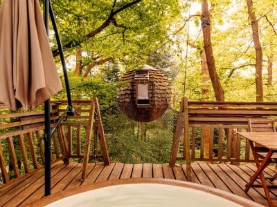 Cabane perchée dans les arbres avec jacuzzi, entourée de verdure apaisante.