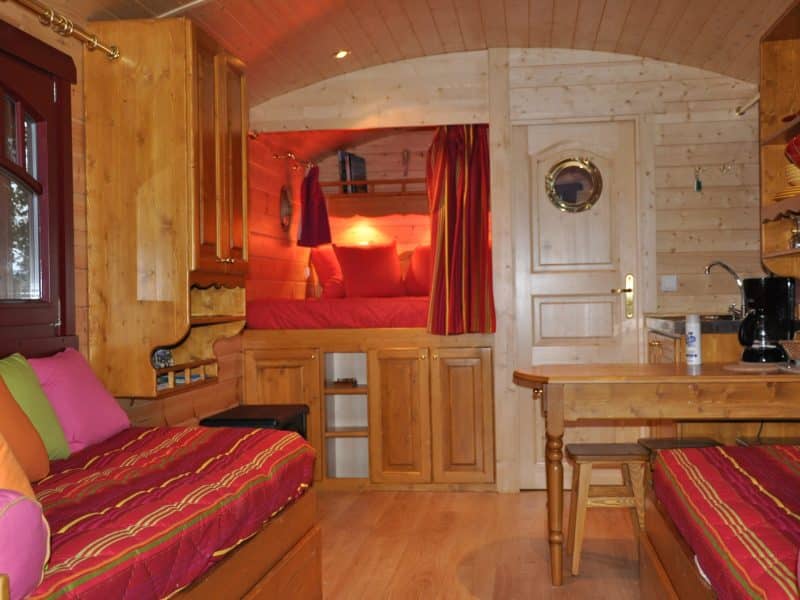 Charmante roulotte en bois avec lits colorés et coin cuisine cosy.