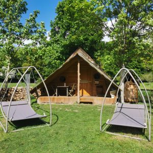 Cabane en bois à Basse-Normandie avec chaises suspendues et verdure environnante.