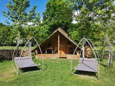Cabane en bois à Basse-Normandie avec chaises suspendues et verdure environnante.