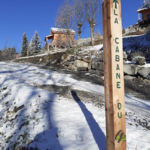 Cabane en bois dans un paysage enneigé, entourée darbres et de montagnes.