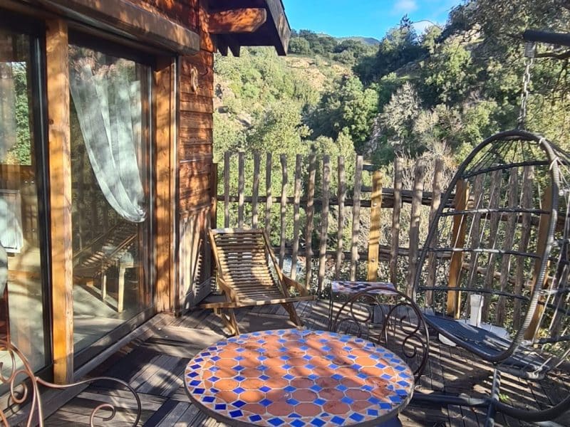 Chalet en bois avec terrasse ensoleillée et table colorée, vue sur la nature.