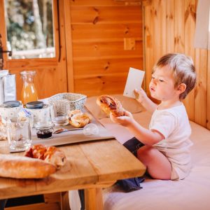 Cabane en bois dans les Pays de la Loire, enfant dégustant un petit-déjeuner copieux.
