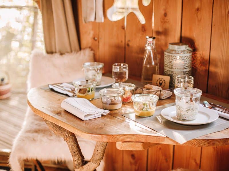Table en bois dans un hébergement insolite, décorée de plats gourmands et de verre.