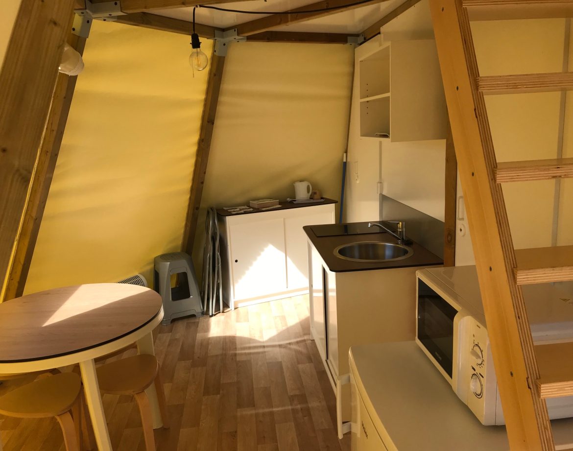 Hébergement insolite en yourte, intérieur lumineux avec cuisine et mobilier en bois.