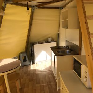 Hébergement insolite en yourte, intérieur lumineux avec cuisine et mobilier en bois.