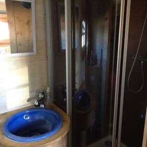Salle de bain dun hébergement insolite en bois avec lavabo bleu et douche moderne.