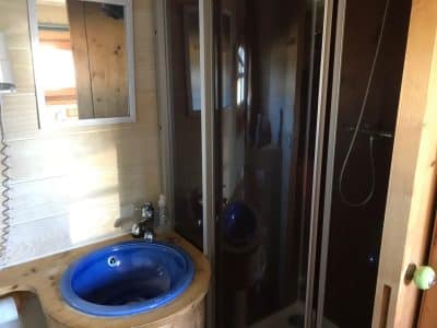 Salle de bain dun hébergement insolite en bois avec lavabo bleu et douche moderne.