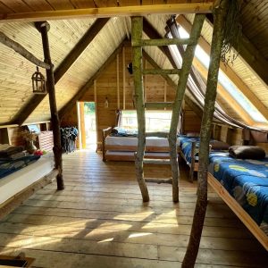 Cabane en bois avec lits simples et lumière naturelle, ambiance chaleureuse et rustique.