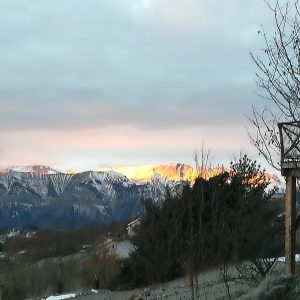 Hébergement insolite en bois avec vue sur les montagnes enneigées au coucher du soleil.
