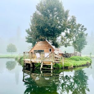 Cabane flottante à Basse-Normandie, entourée deau et de verdure, ambiance paisible.