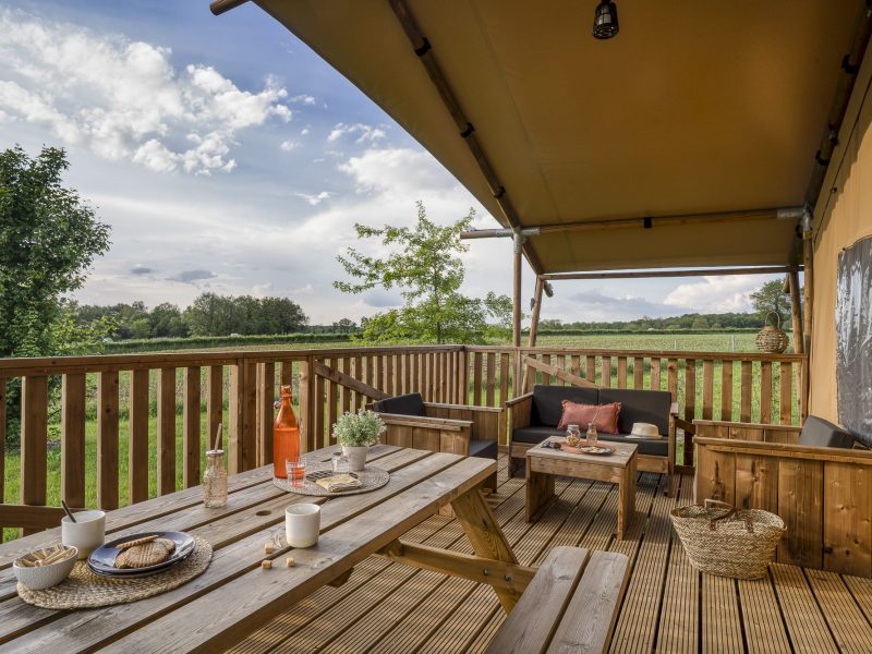 Hébergement insolite en toile avec terrasse en bois, vue sur la nature verdoyante.