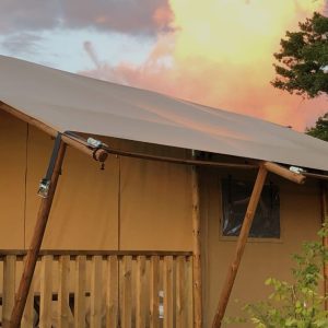 Tente safari en bois avec terrasse, face à un ciel coloré au coucher du soleil.