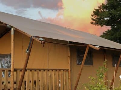 Tente safari en bois avec terrasse, face à un ciel coloré au coucher du soleil.