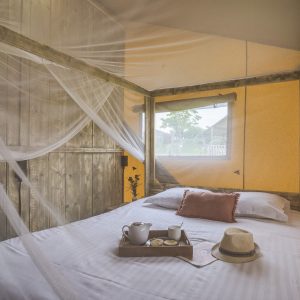 Chambre en cabane avec moustiquaire, décor chaleureux et vue sur la nature.