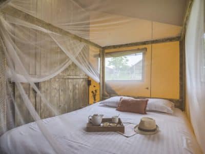 Chambre en cabane avec moustiquaire, décor chaleureux et vue sur la nature.