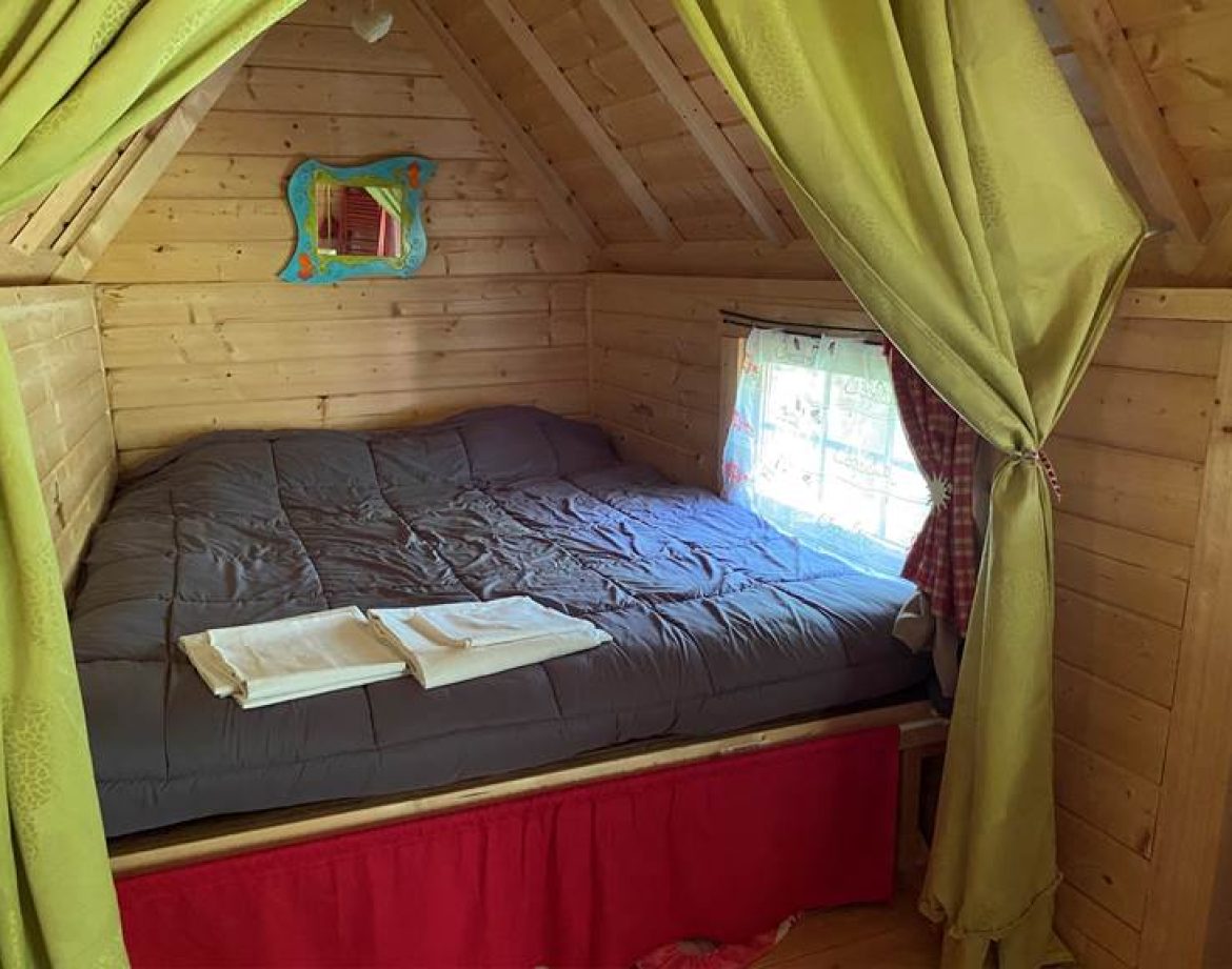 Cabane en bois cosy avec lit douillet et rideaux colorés à Centre.