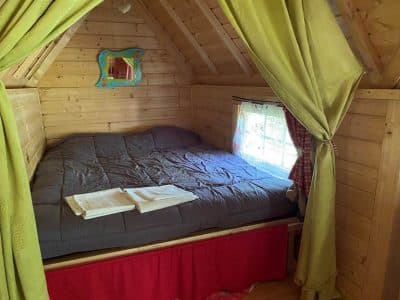 Cabane en bois cosy avec lit douillet et rideaux colorés à Centre.
