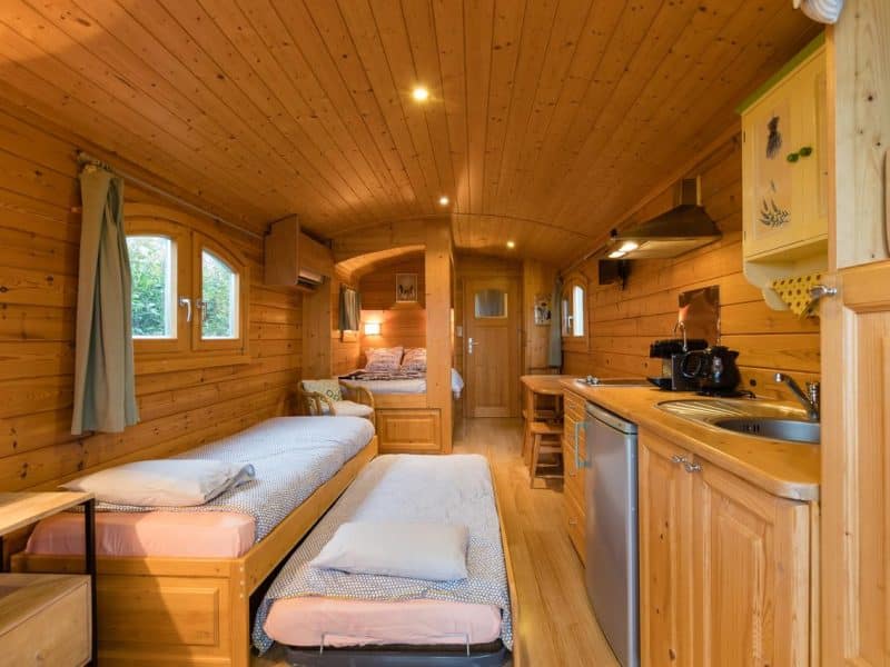 Charmante roulotte en bois, intérieur chaleureux avec lits confortables et cuisine équipée.
