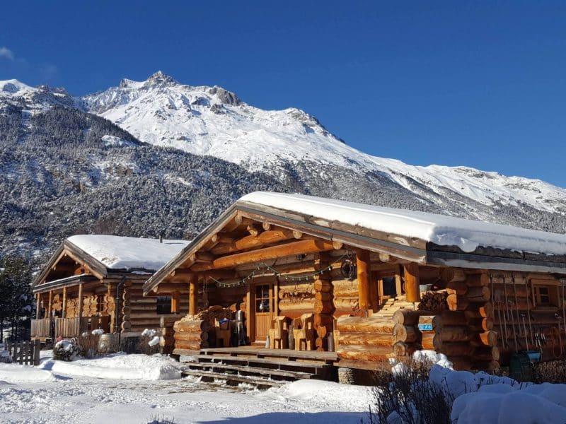 Chalet en bois dans un paysage alpin enneigé, entouré de montagnes majestueuses.