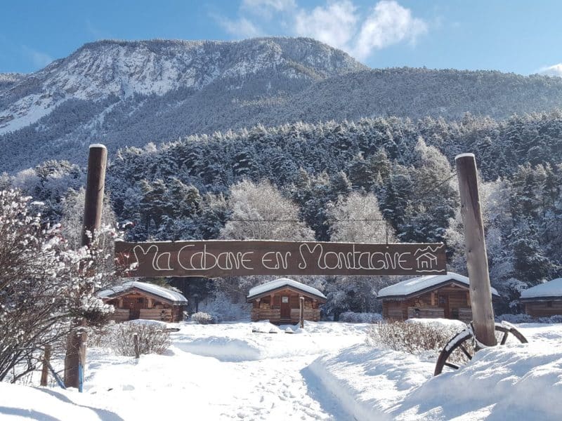 Chalets en bois sous la neige, entourés de montagnes majestueuses.
