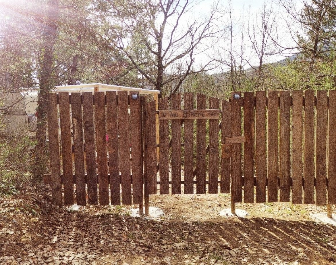 Cabane en bois dans la nature, entourée darbres et dun portail en bois rustique.