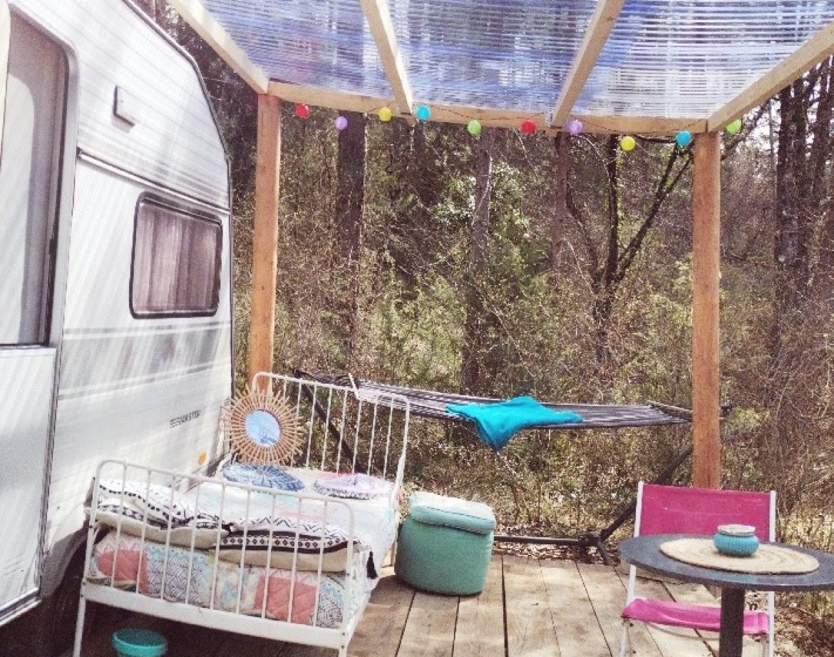 Caravane vintage avec terrasse en bois, décorée de guirlandes lumineuses.
