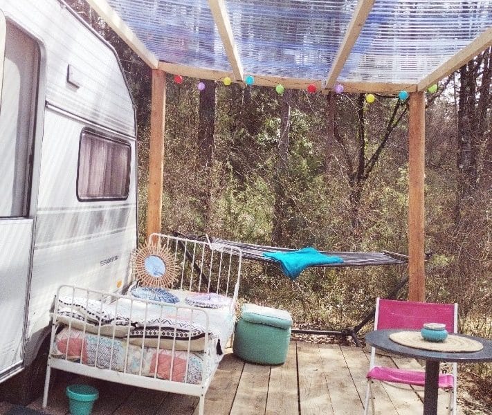 Caravane vintage avec terrasse en bois, décorée de guirlandes lumineuses.