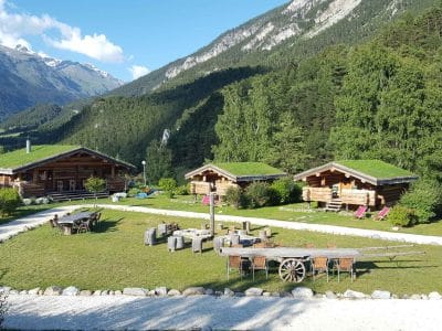 Chalets en bois avec toit végétal, entourés de verdure et montagnes majestueuses.